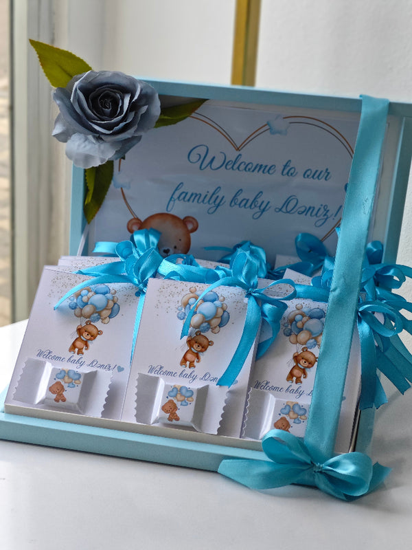 Baby shower gift set with teddy bear design and blue ribbons on a white surface.