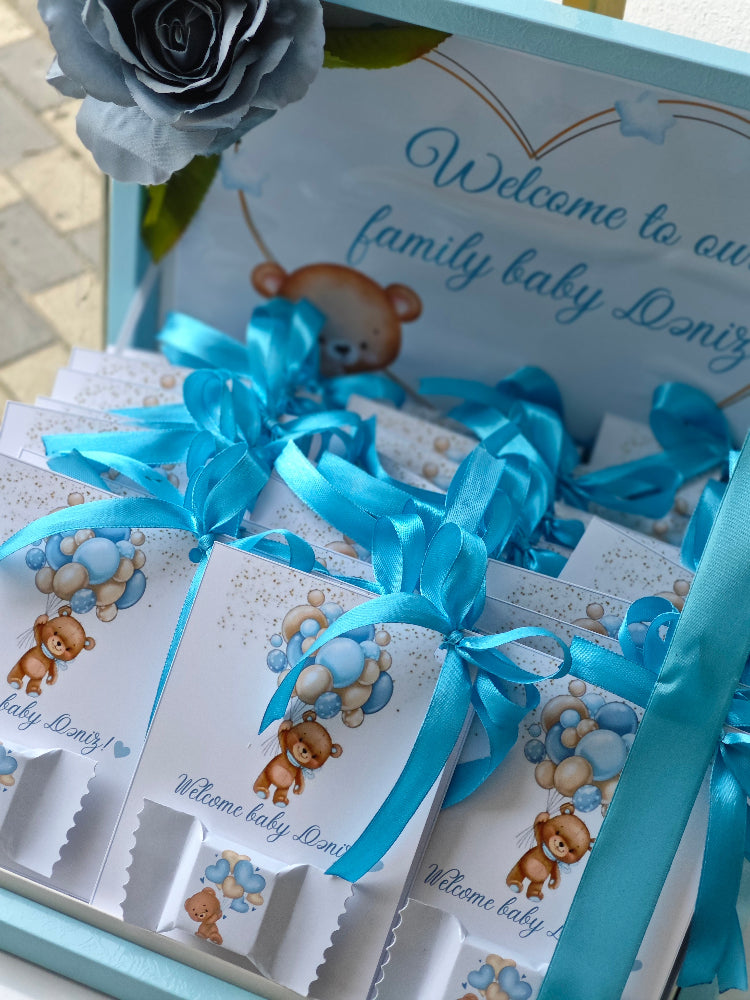 Baby shower gift set with teddy bear design and blue ribbons on a light blue box.