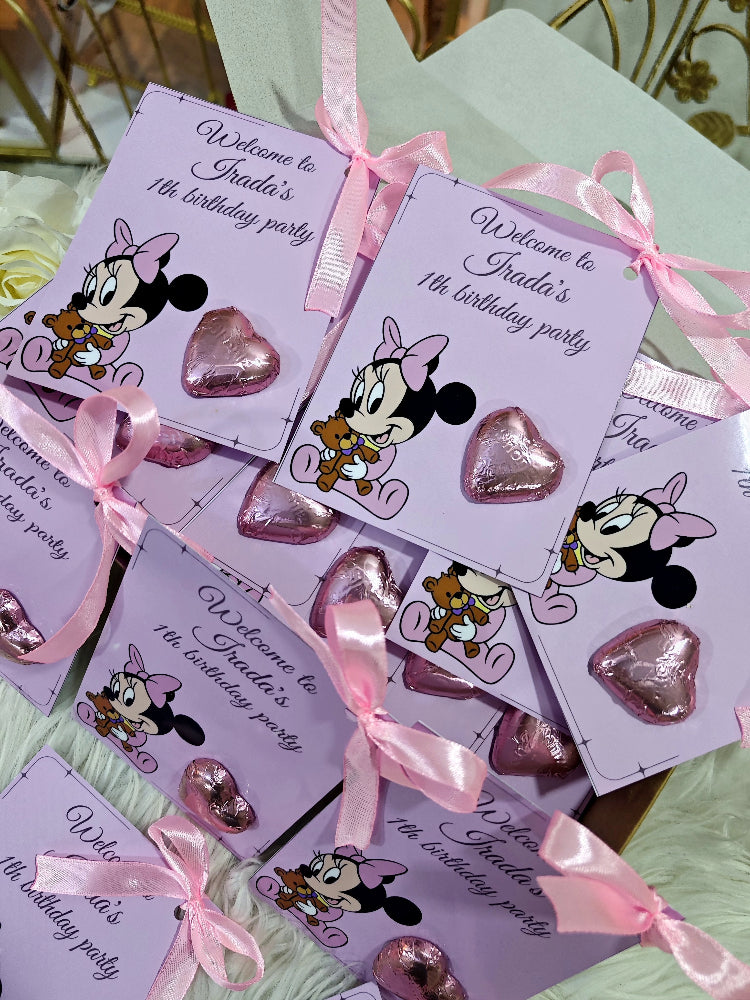 Minnie Mouse-themed party favors with pink ribbons and heart-shaped candies on a white surface.
