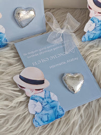 Heart-shaped earrings on a blue card with a decorative bow, placed on a textured surface.