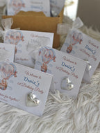 Party favors with heart-shaped decorations and 'Welcome to Deniz's 1st Birthday Party' text on a fluffy white surface.