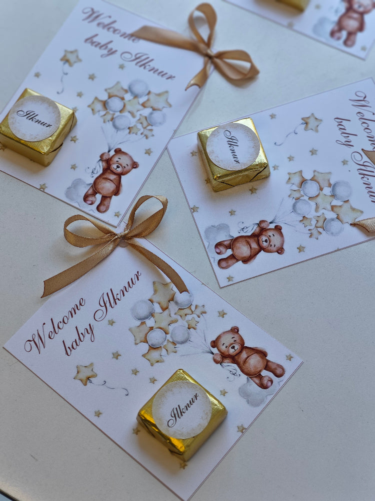 Baby shower invitations with teddy bear illustrations and gold candy bars on a light surface.