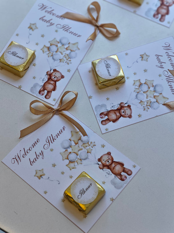 Baby shower invitations with teddy bear illustrations and gold candy bars on a light surface.