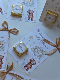 Gold baby shower favor boxes with ribbons and teddy bear designs on cards.