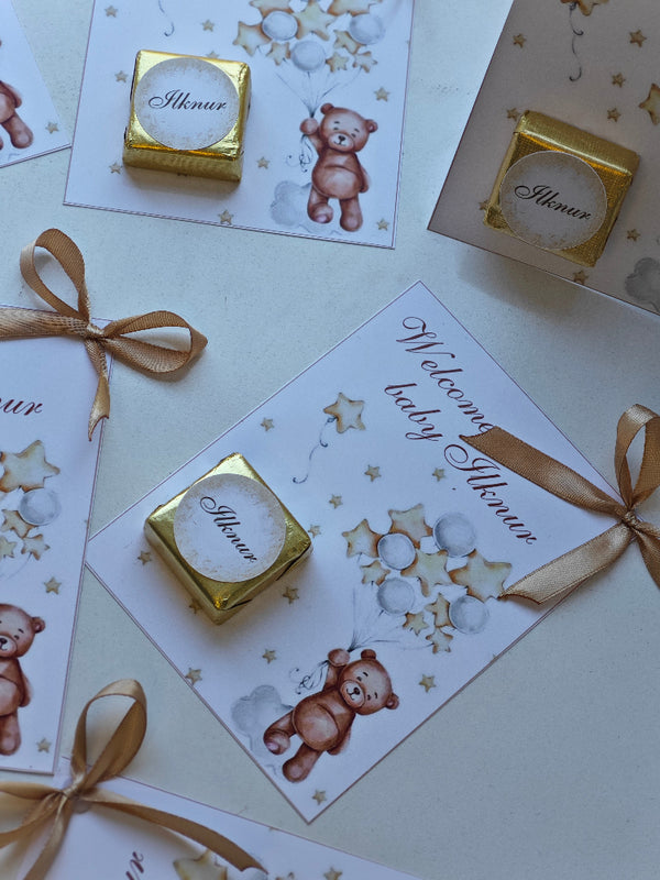 Gold baby shower favor boxes with ribbons and teddy bear designs on cards.
