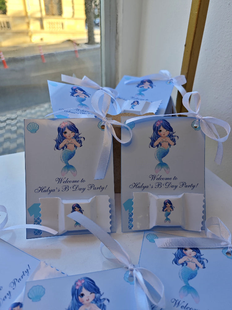 Mermaid-themed birthday party decorations with cards and ribbons on a table.