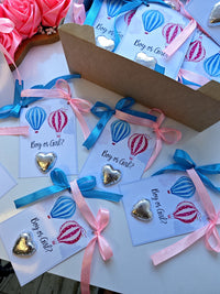 Heart-shaped chocolate candies with 'Boy or Girl?' tags and ribbons in a box.