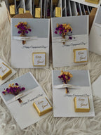 Engagement card with gold box and dried flowers on a textured surface