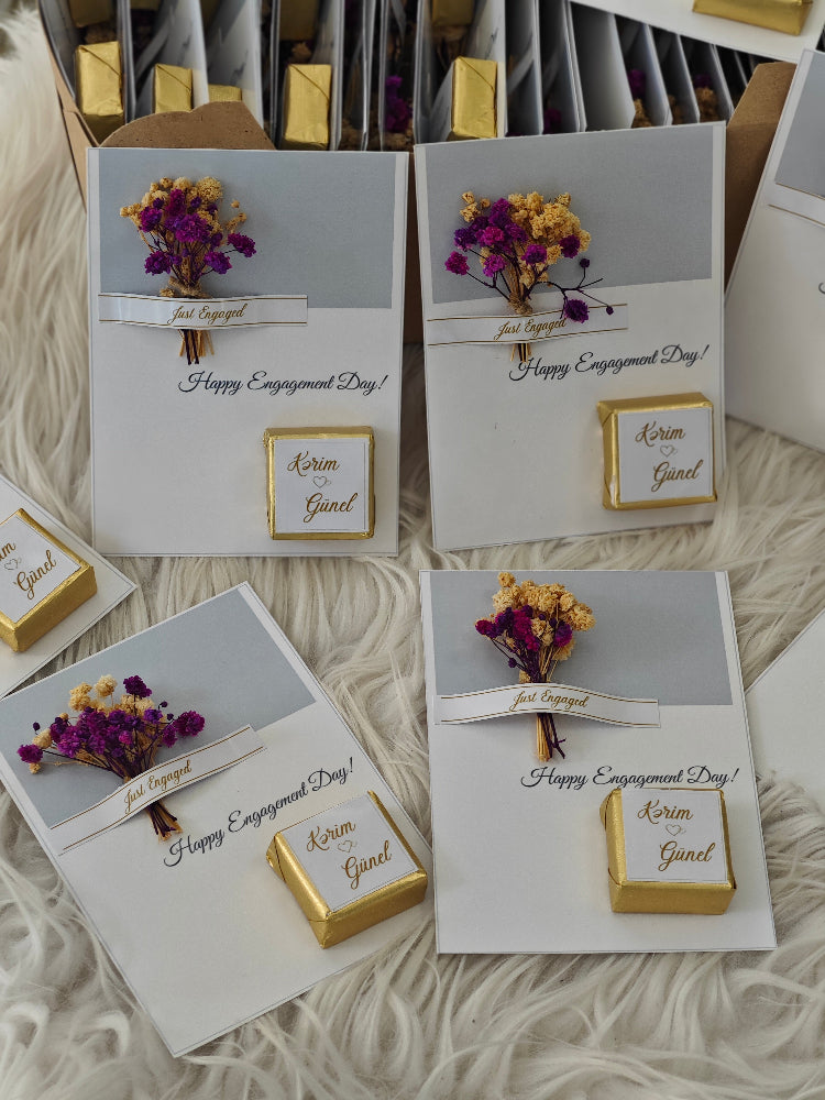 Engagement card with gold box and dried flowers on a textured surface