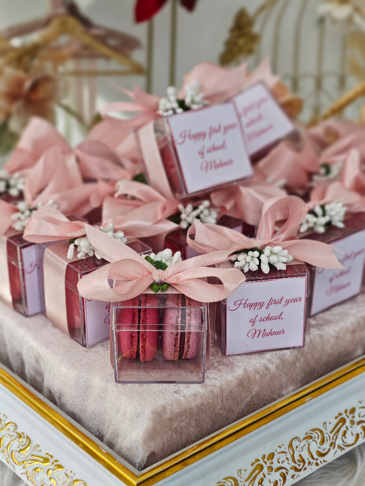 Decorative boxes with pink ribbons and macarons on a decorative stand.