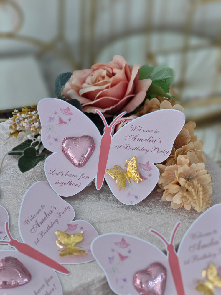 Butterfly-shaped birthday party invitations with floral decorations on a table.