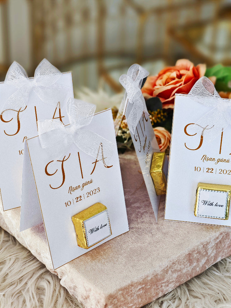 White cards with gold text and ribbons on a decorative surface with flowers in the background