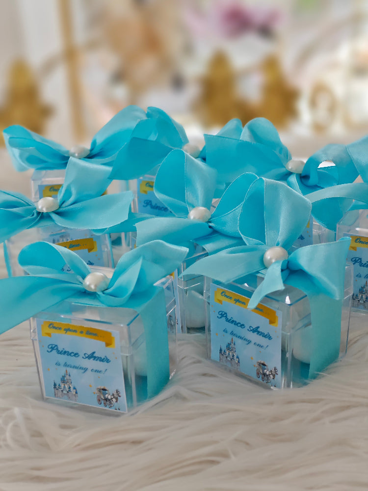 Small clear containers with blue ribbons and 'Prince' labels on a textured surface.