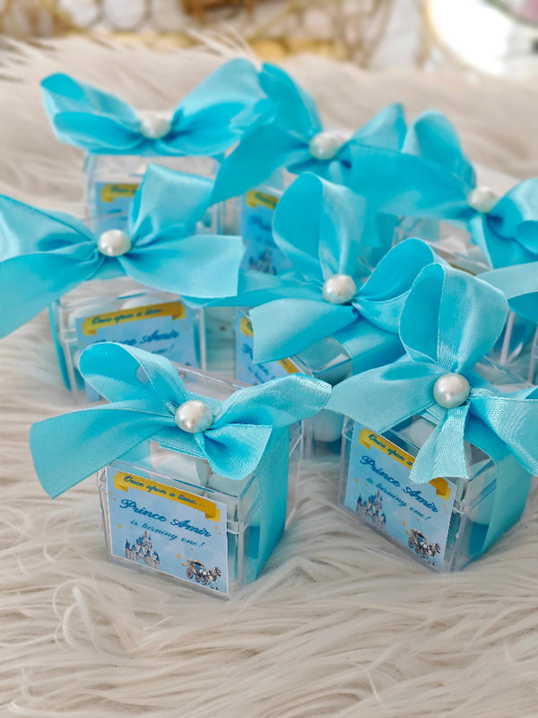 Small clear boxes with blue ribbons and pearls on a textured surface