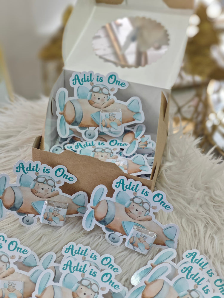 Set of 'Addil is One' stickers with a bear design on a cardboard stand.