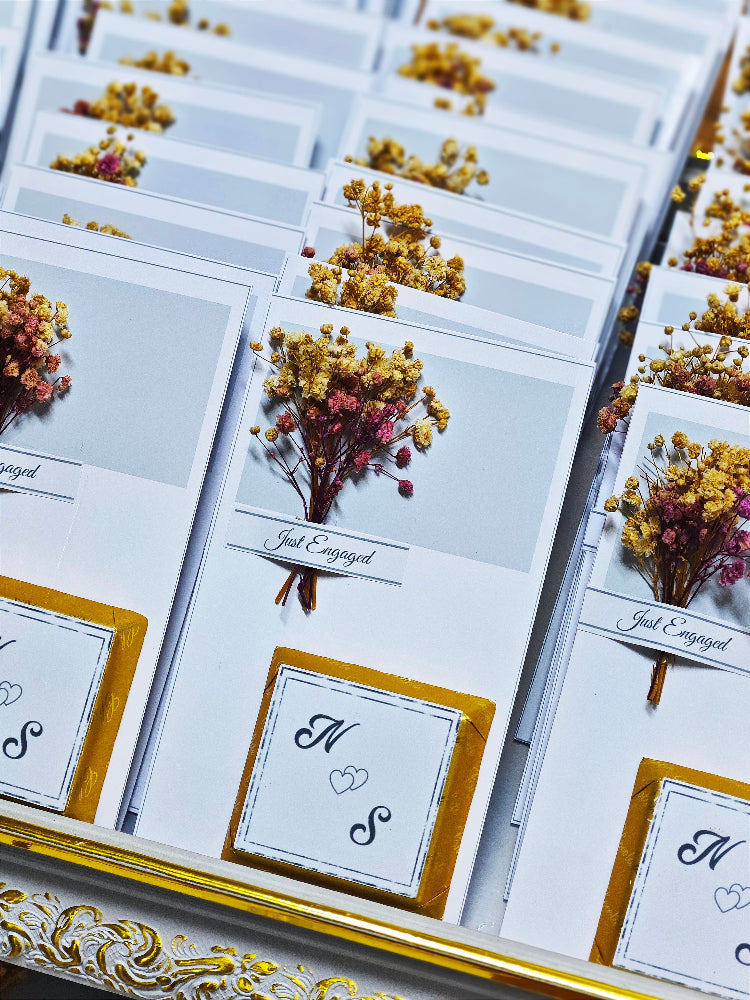 Engagement cards with dried flowers and initials on a decorative surface