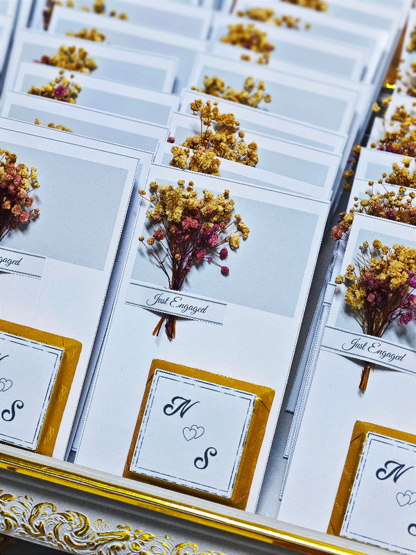 Engagement cards with dried flowers and initials on a decorative surface
