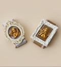 Two decorative wall art pieces with gold figures in ornate frames on a textured surface.