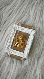 Decorative wall art with a gold angel figure in a white frame on a textured surface