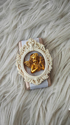 Decorative item with gold angel figure in an ornate white frame on a textured surface
