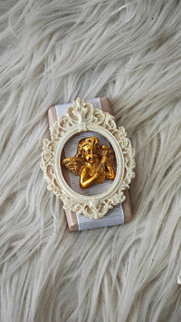 Decorative item with gold angel figure in an ornate white frame on a textured surface