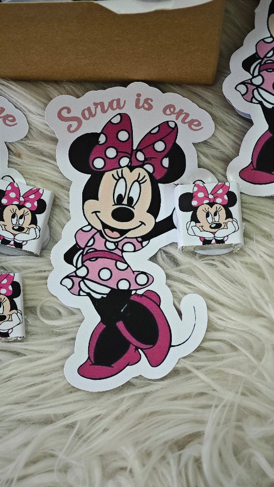 Minnie Mouse-themed birthday card with 'Sara is one' text on a textured surface.