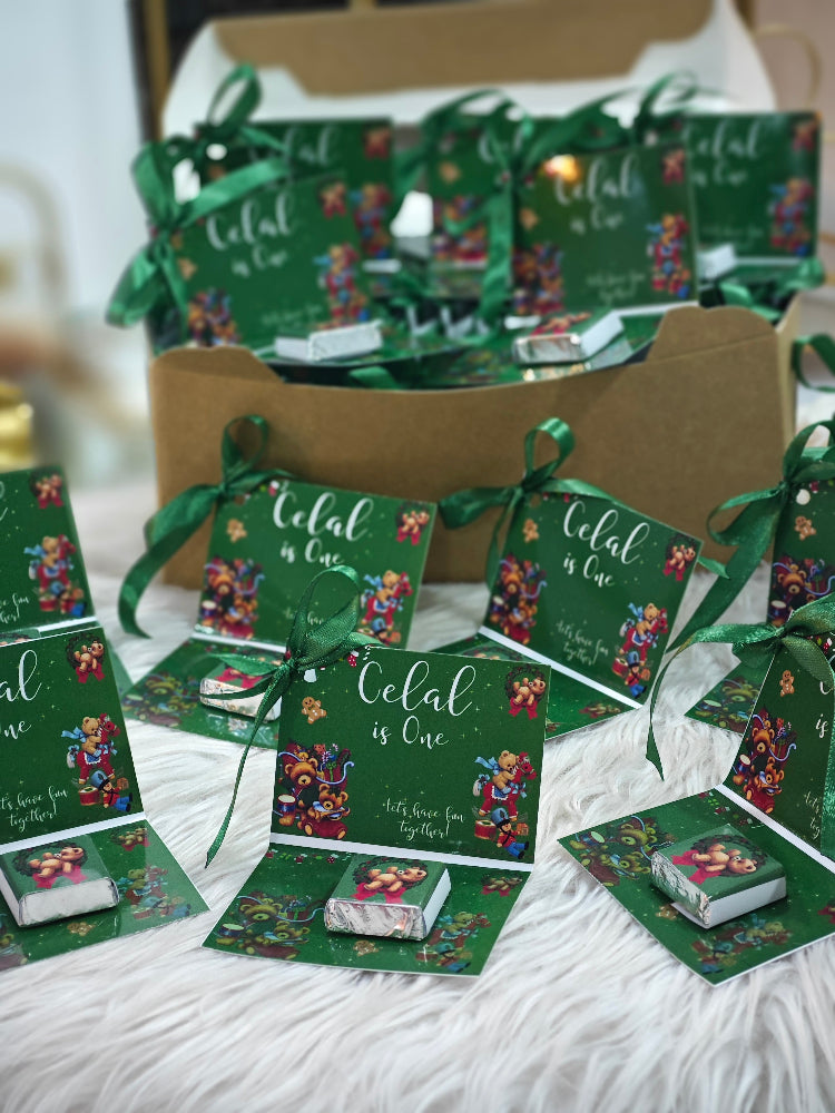 Green party favor boxes with ribbons and 'Colal is One' text on a white surface.