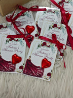 Invitations for a Henna Party with red ribbons and heart decorations on a textured surface.