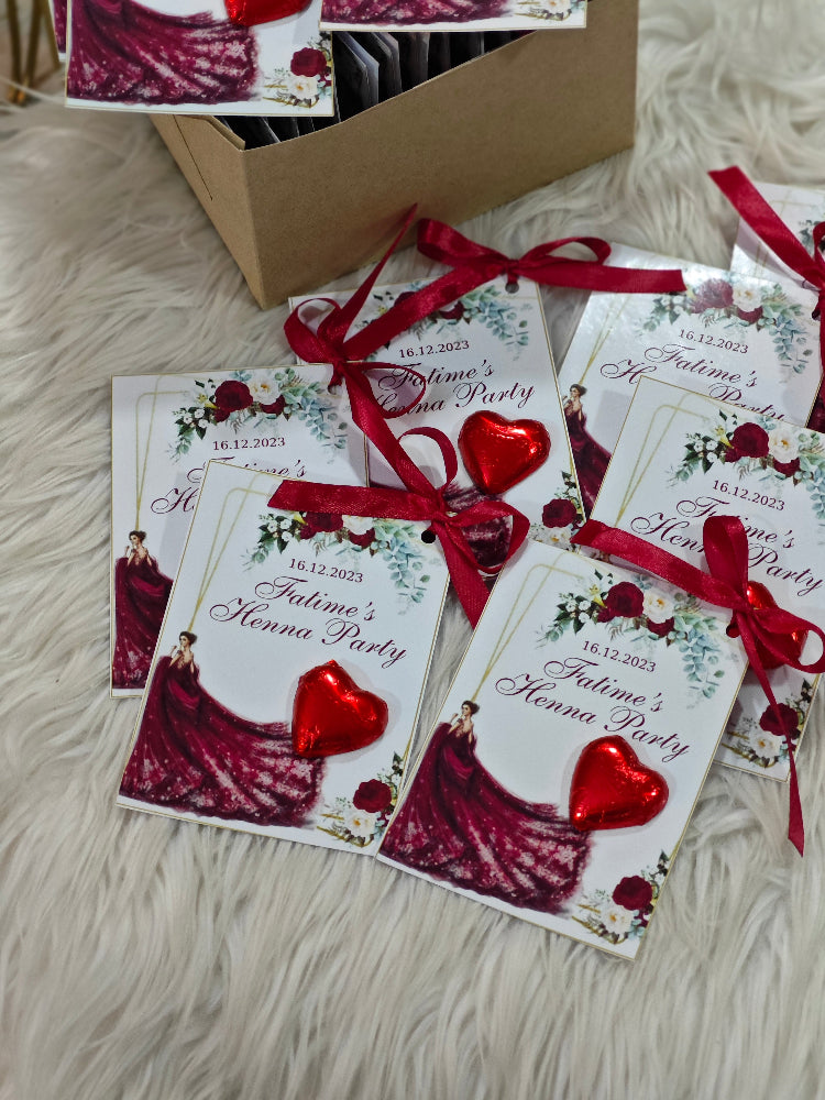 Invitations for a 'Paloma's Hen Party' with red ribbons and heart decorations on a fluffy surface.