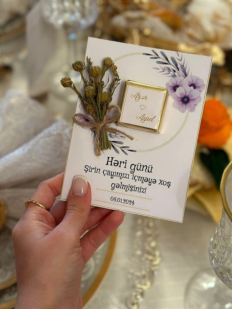 Hand holding a card with floral decorations and text on a blurred background