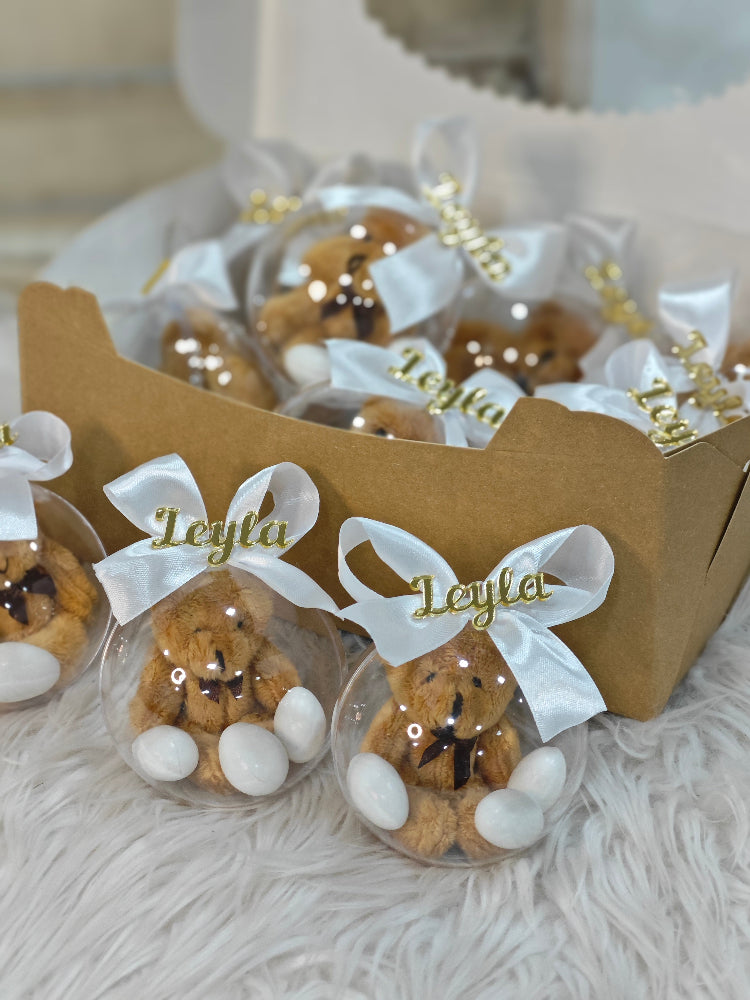 Teddy bears in clear plastic bags with white ribbons and 'Leyla' branding, inside a cardboard box.