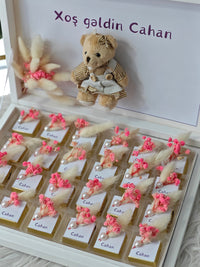 Decorative box with teddy bear, flowers, and name cards on a white background