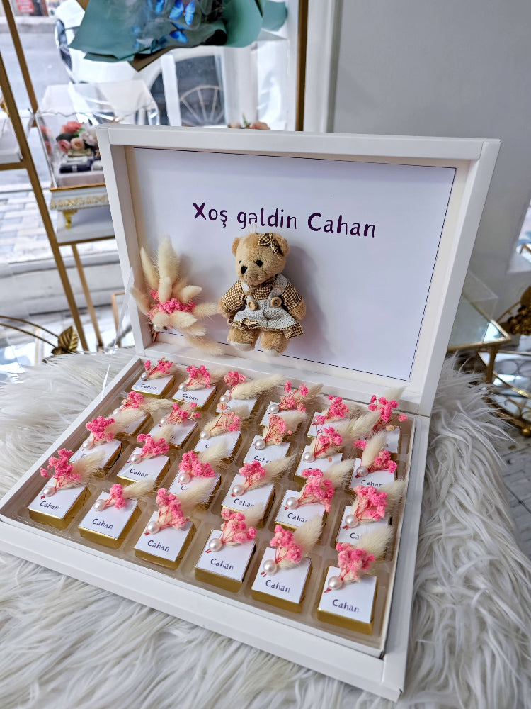 Decorative box with teddy bear, flowers, and personalized text on a light background