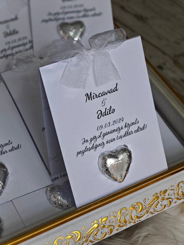 Heart-shaped chocolate in a decorative box with a white ribbon and personalized card.