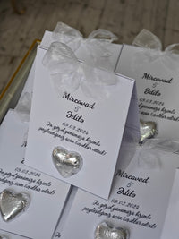 Silver heart-shaped earrings in packaging with personalized text on a wooden surface.