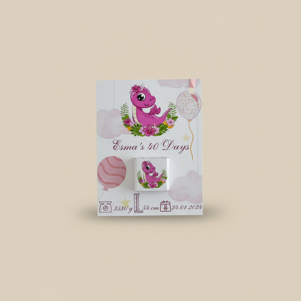 Pink dinosaur-themed baby shower favor boxes with ribbons on a wooden surface.