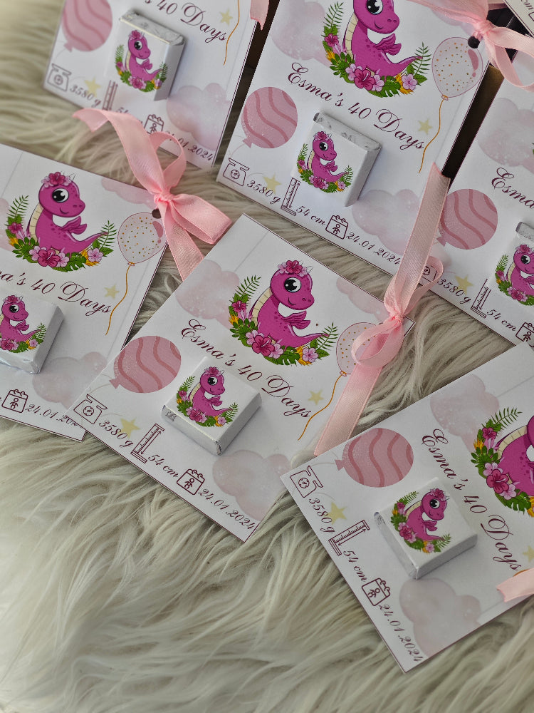Set of baby shower favor boxes with pink dinosaur design on a fluffy white surface