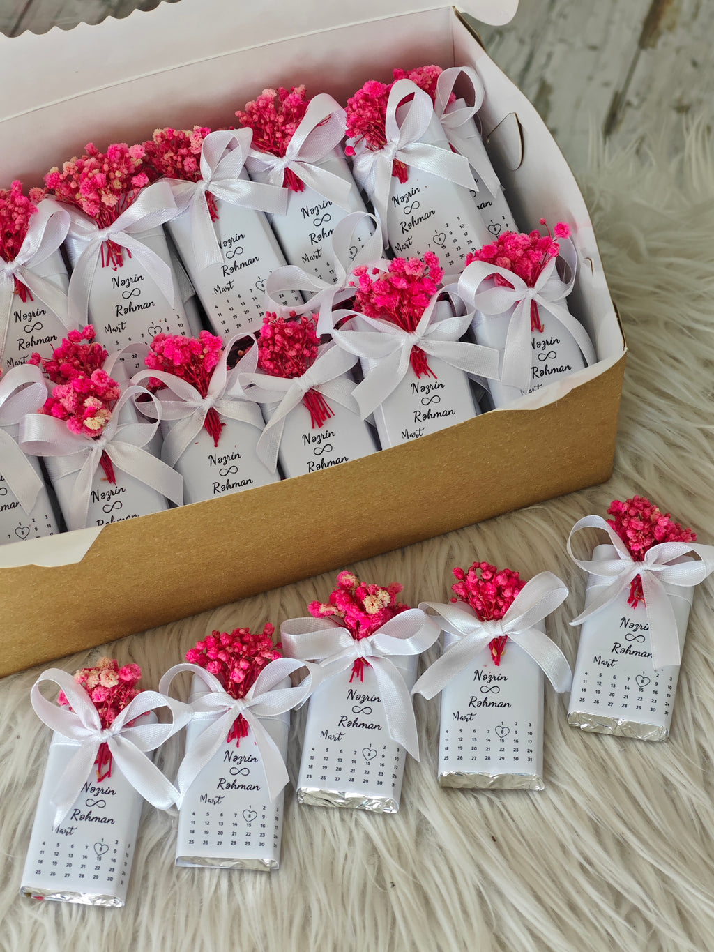 Small packages with pink flowers and white ribbons arranged in a box.