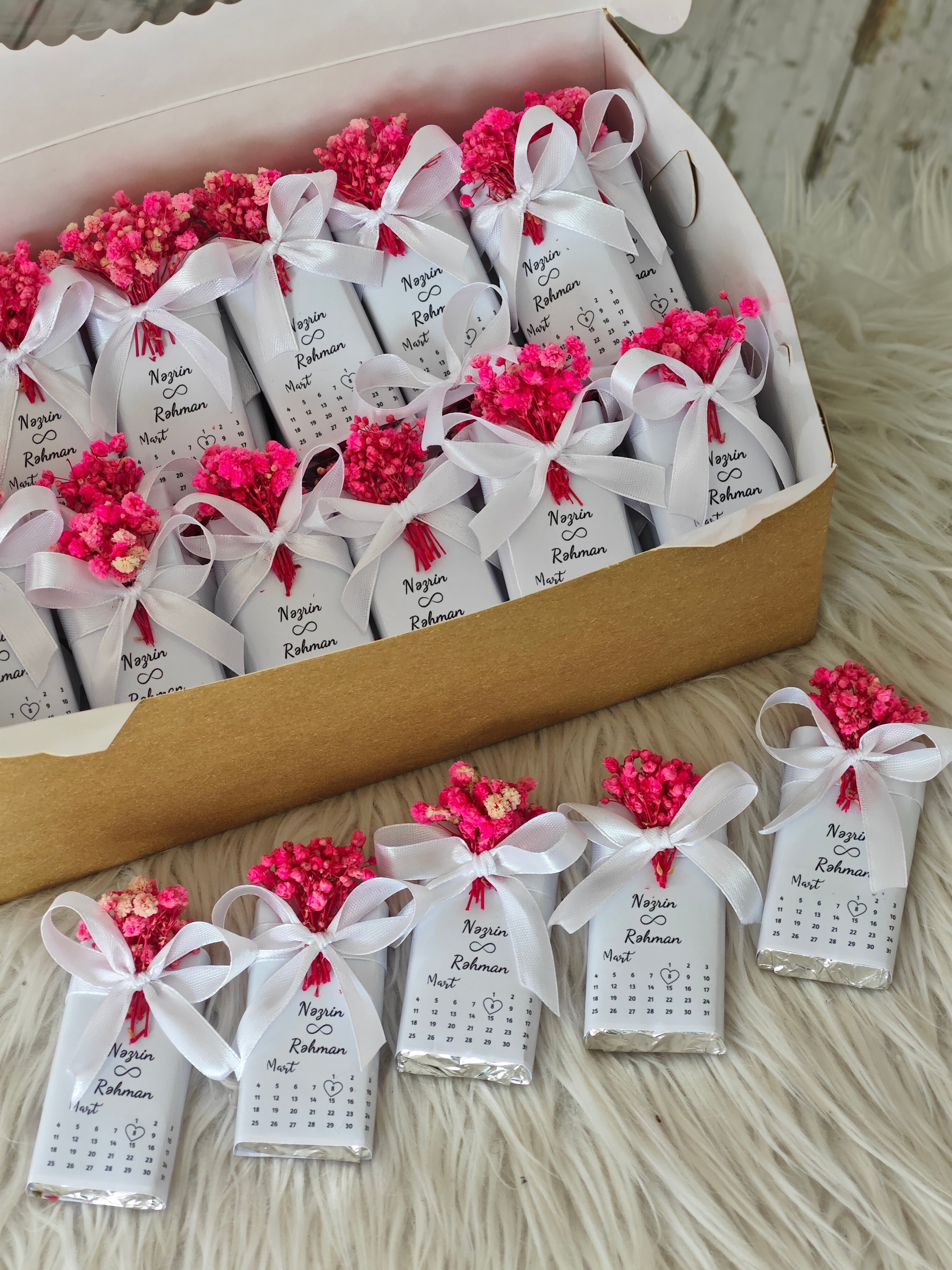 Small packages with pink flowers and white ribbons arranged in a box.