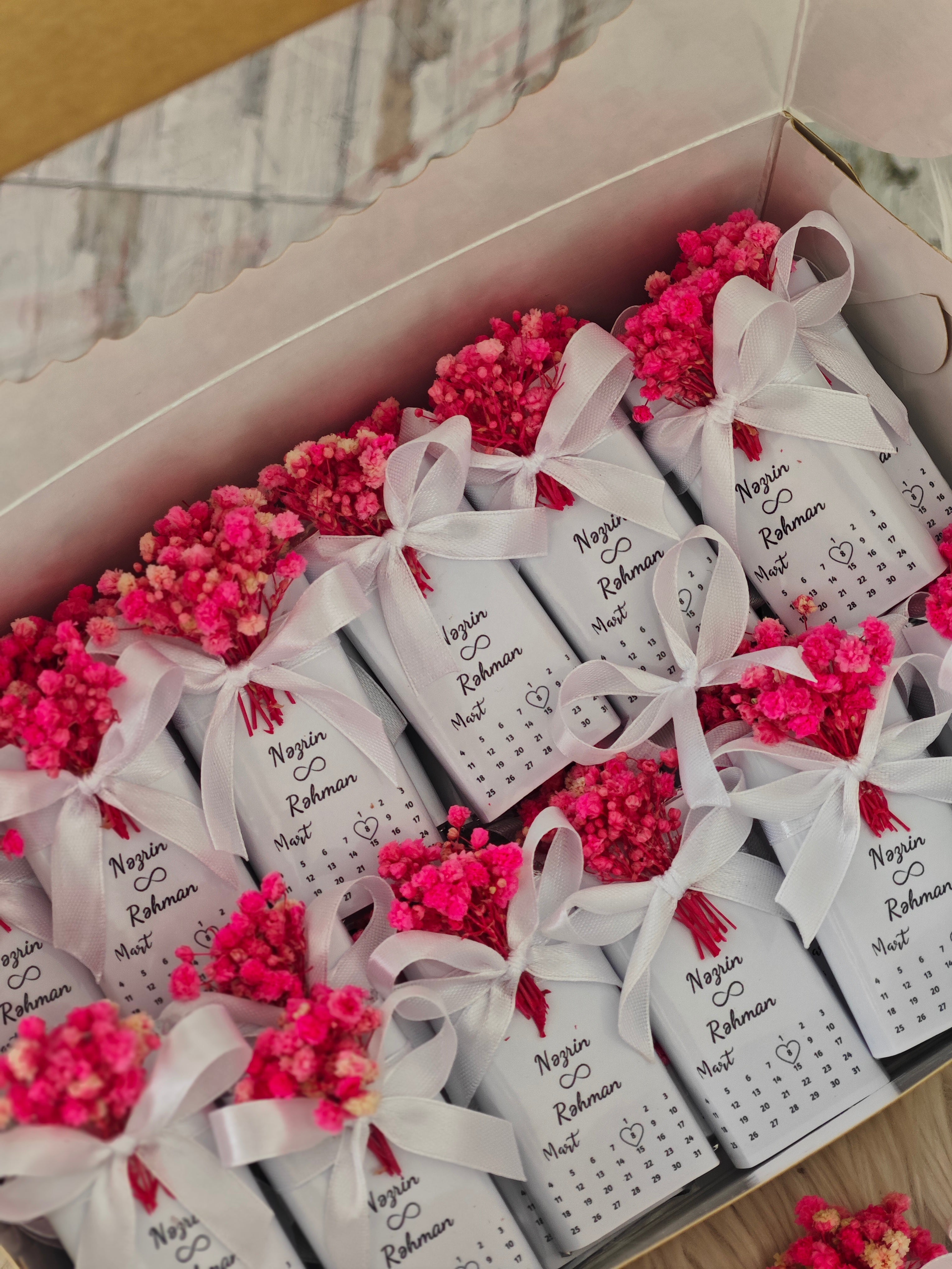 Box of white gift bags with pink flowers and names on a wooden surface