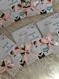 Wedding invitations with cartoon couple and pink ribbons on a textured surface