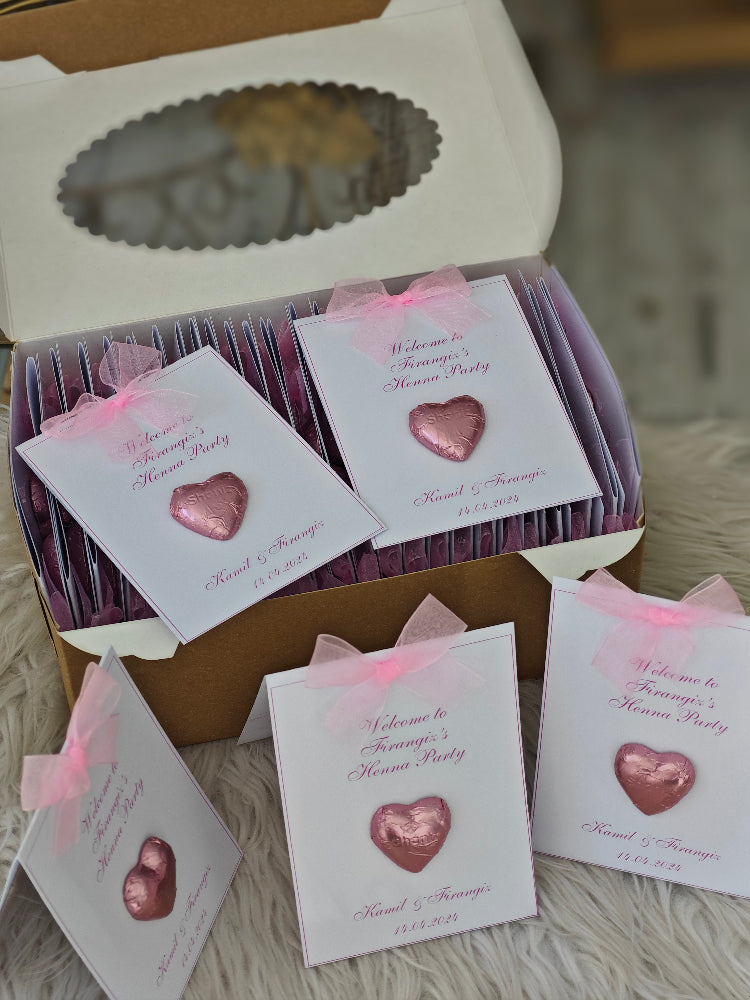 Box of pink heart-shaped favors with personalized cards on a textured surface.