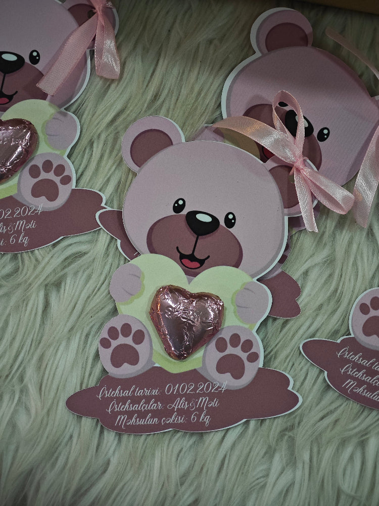 Card with a teddy bear design holding a heart on a textured green surface