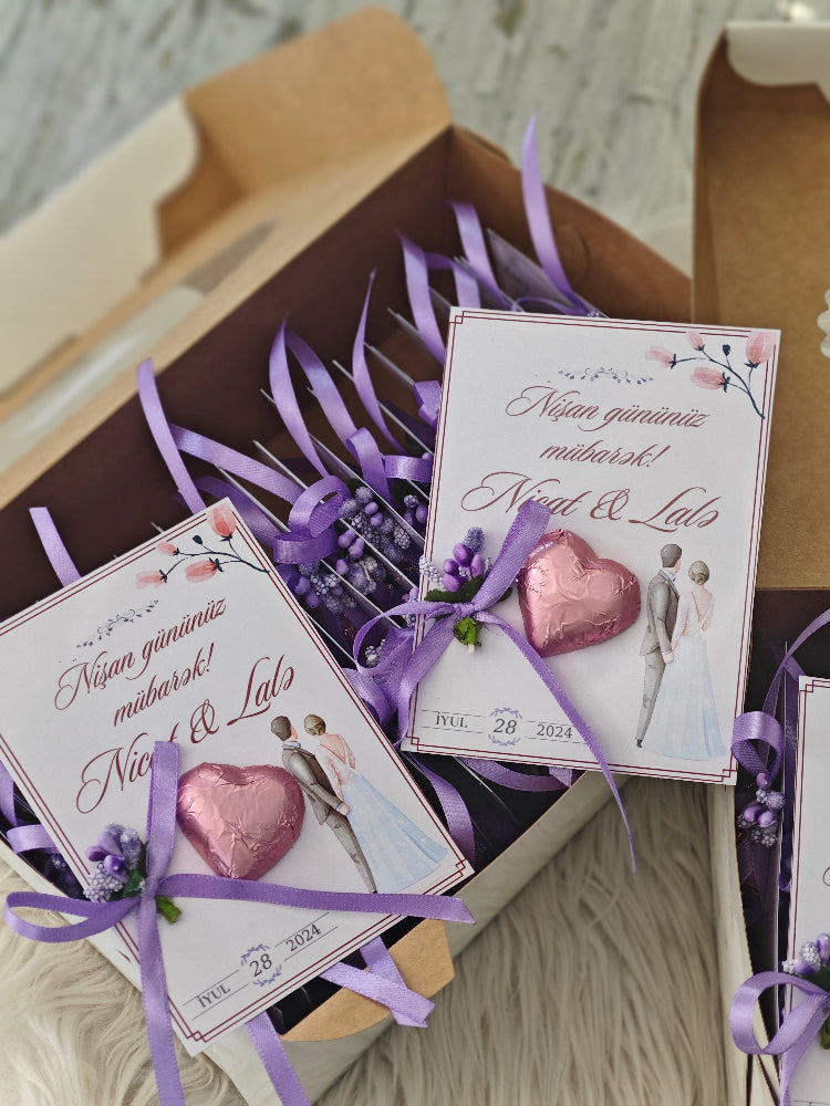 Two small boxes with heart-shaped pink candies and purple ribbons on a wooden surface.