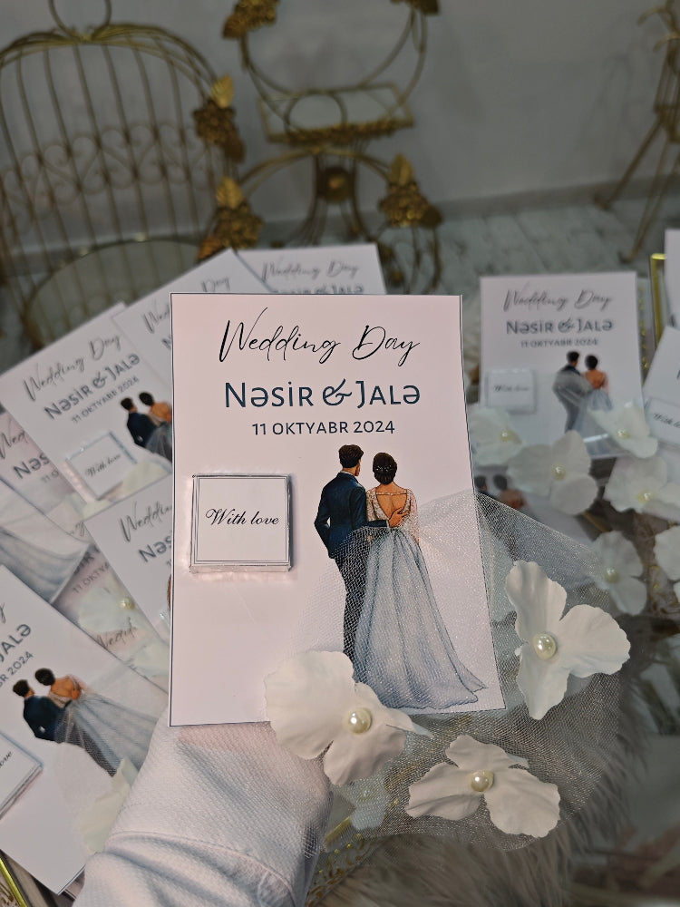 Wedding invitation card with a couple's photo and text, surrounded by decorative flowers on a glass surface.