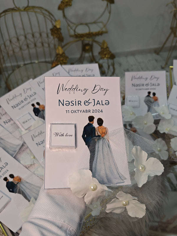 Wedding invitation card with a couple's photo and text, surrounded by decorative flowers on a glass surface.