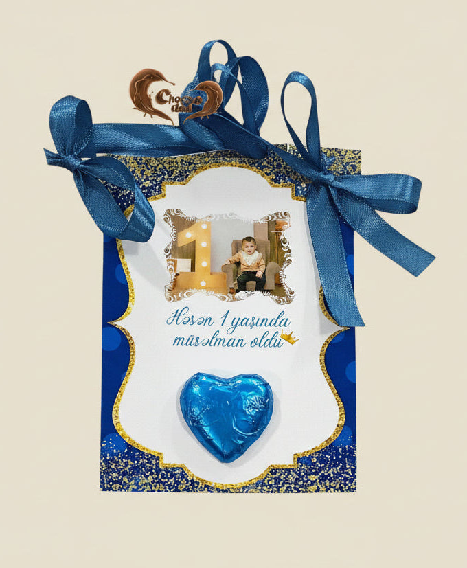 Decorative box with blue ribbon, heart-shaped chocolate, and photo of a child on a white background
