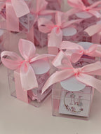 Clear gift boxes with pink ribbons and decorative tags on a light background