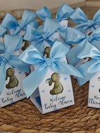 Small boxes with blue ribbons and baby-themed illustrations on a woven surface