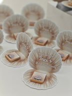 Seashell-shaped party favors with 'Welcome to Inci's 1st Birthday Party' text on a white surface.